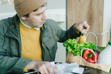 Mindful man scanning multiple receipts, comparing store prices, and maintaining healthy grocery...