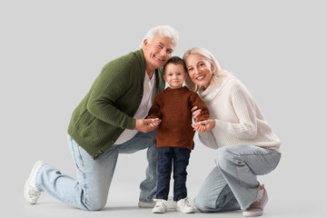 Cute little boy with happy grandparents in warm sweaters on grey background