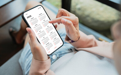 Businesswoman using smartphone with monthly calendar to plan 2025 activities. Scheduling and...