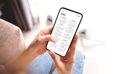 Businesswoman using smartphone with monthly calendar to plan 2025 activities. Scheduling and...