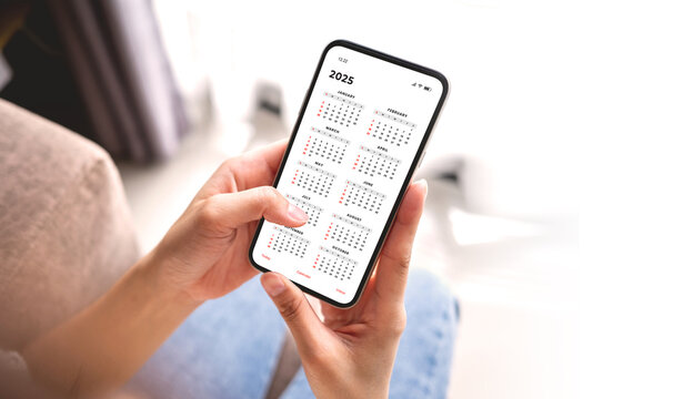 Businesswoman using smartphone with monthly calendar to plan 2025 activities. Scheduling and organizing plans. Technology and business concept.