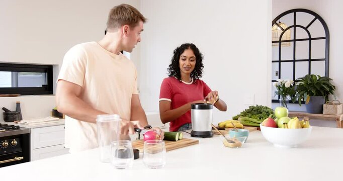 Preparing fresh smoothie, young multiracial couple cutting fruits and vegetables in kitchen, at home - Powered by Adobe