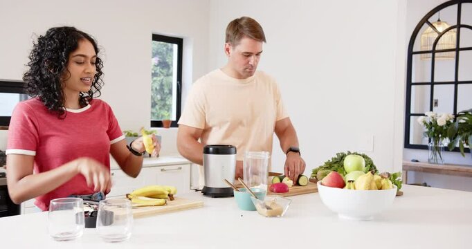 Preparing healthy smoothie, young multiracial couple cutting fruits and vegetables, at home - Powered by Adobe