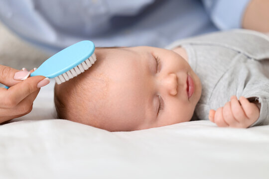 Mother brushing her sleeping little baby's head with cradle cap on bed, closeup