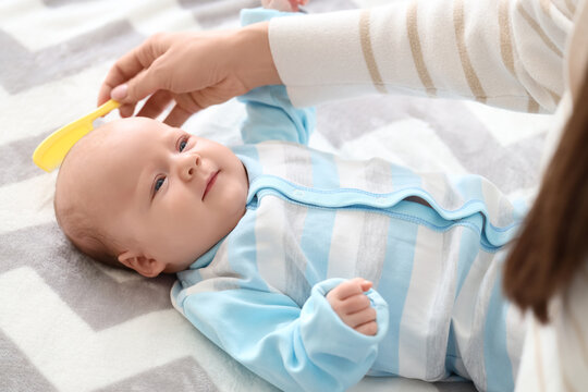 Woman combing her little baby's hair with cradle cap on bed, closeup - Powered by Adobe