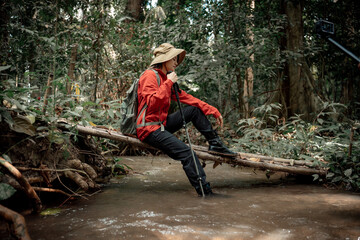 Hiker with sitting with stick crossing small bridge forest wearing backpacks, indicating on a...