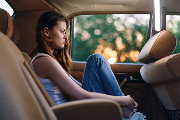 Thoughtful young woman sitting in a car during sunset, reflecting on life in a serene moment, wearing casual clothing and lost in deep contemplation.