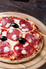 Pizza with salami and mozzarella cheese. Wooden background. Soft focus. Close up.