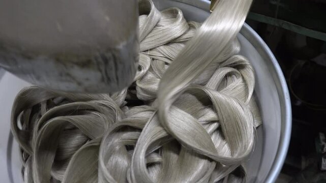 Linen rope processing machine feeding processed fibers through a metal chute into a yellow container below, in an industrial setting.