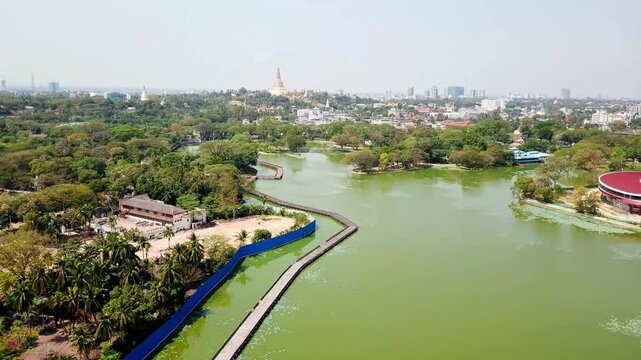 A breathtaking aerial view of Kandawgyi Lake and its lush surroundings with the iconic Shwedagon Pagoda in Rangun, Myanmar. The scene features vibrant greenery, water reflections, and urban highlights