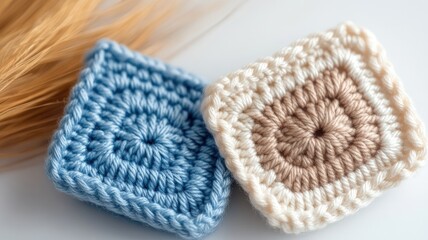 Two crocheted square coasters in blue and beige, placed alongside wheat strands