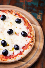 Pizza with mozzarella cheese and black olives on wooden background. Soft focus. Close up