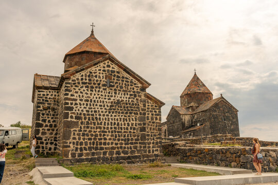 A stone building with a cross on top. A woman is standing in front of it. The building is old and has a Gothic style