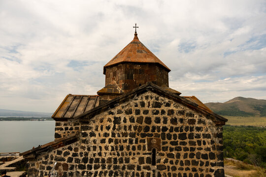 A stone building with a steeple and a cross on top. The building is surrounded by trees and a body of water