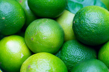 close-up of fresh, whole green limes with glossy, textured surfaces. The fruits are piled together,