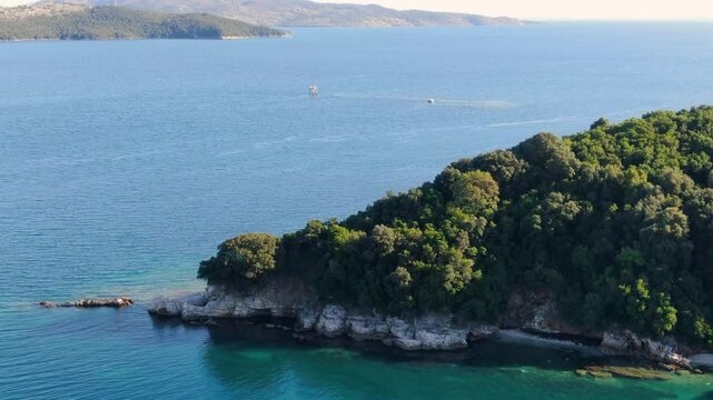 Aerial view of a lush green peninsula jutting into a vibrant turquoise sea. erimitis corfu greece