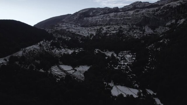 This drone video features a stunning reverse descriptive shot over the Hecho Valley in the Aragonese Pyrenees, Spain, revealing snowy mountains at sunset under a cloudy sky, creating a dramatic scene.