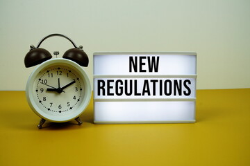 New Regulations text on LED lightbox with alarm clock on yellow background