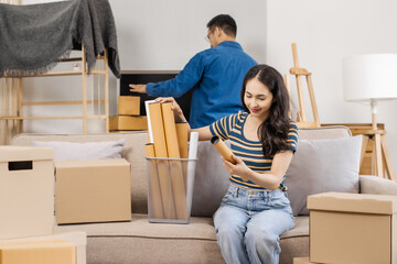 Young couple sitting on a sofa, helping each other pack, collecting clothes, putting items in...