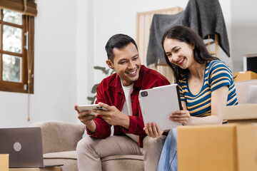 Young couple sitting on the sofa in their new house, happily using a laptop, enjoying each other's company, and creating joyful memories in their fresh, cozy home environment