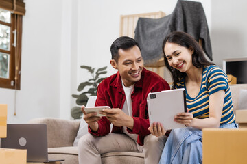 Young couple sitting on the sofa in their new house, happily using a laptop, enjoying each other's company, and creating joyful memories in their fresh, cozy home environment