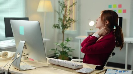 Young asian businesswoman experiencing neck pain while working on computer, massaging her neck and shoulders to relieve tension and discomfort caused by long hours of sitting in office