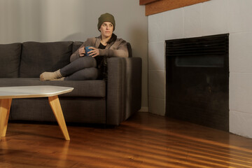A person relaxes on a sofa with a mug near a cozy fireplace