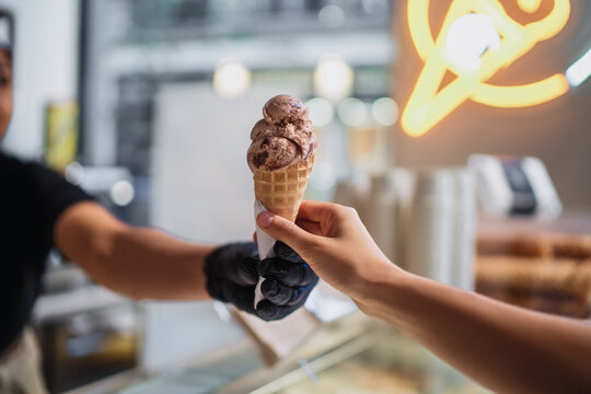 Ice cream shop worker serving chocolate ice cream cone to customer