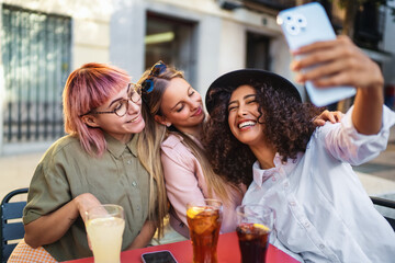 Three happy friends taking a selfie while having drinks at outdoor cafe