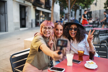Three young women taking a selfie while having drinks at outdoor cafe