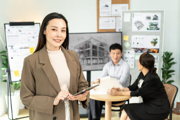 Confident businesswoman holding a tablet with team discussing architectural project in modern office workspace