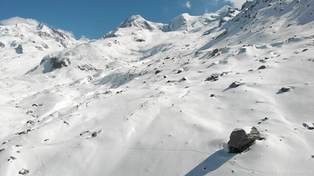 Aerial flyover view of a skier next to snow covered Gorner glacier in Zermatt, Switzerland on a sunny winter next to the tallest peaks of the Swiss Alps with a view of Monte Rosa, ice and moraines.