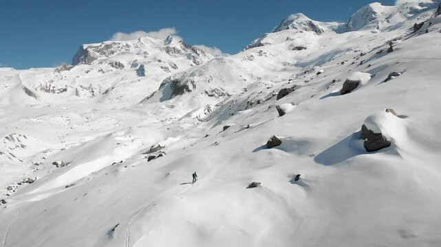 Aerial view of a skier on a ski tour next to Gorner glacier in Zermatt, Switzerland covered in snow on a sunny winter day with a view of the tallest peaks of the Swiss Alps including Monte Rosa.