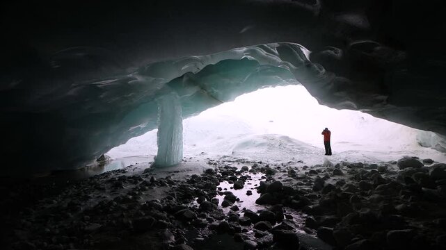 A winter adventurer with a camera climbs out of the darkness of a glacier cave in the Swiss Alps after inspecting the ice of a giant frozen icicle and taking photos