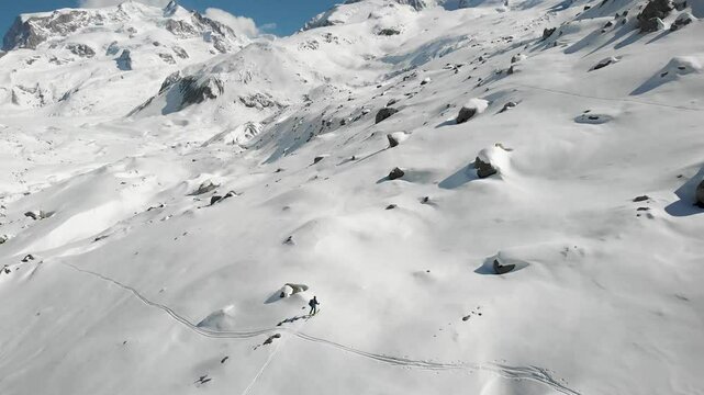 Aerial view of a skier on a ski tour adventure with a view of snow covered Gorner glacier in Zermatt, Switzerland on a sunny winter day next to the tallest peaks of the Swiss Alps including Monte Rosa