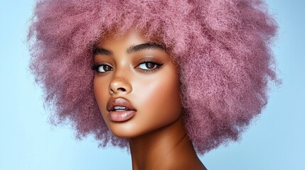 Fototapeta premium young model with a stunning pink curly hairstyle poses confidently. soft blue background enhances her radiant skin and striking facial features, creating an artistic and modern look