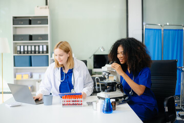 Fototapeta premium Focused Female doctor and African female nurse look at tablet and laptop screen discuss anamnesis together.