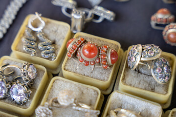 A collection of rings and earrings are displayed in a box. The earrings are of various shapes and sizes, and the rings are also diverse in design. Scene is one of abundance and variety