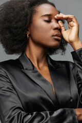Elegant African woman in a black satin suit expressing deep thought against a neutral gray...