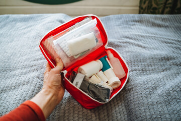 A person is carefully holding a first aid kit on a bed, ensuring that all the necessary items for personal care and emergencies are readily accessible within the kit for any potential needs