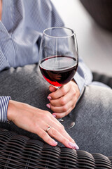 A glass of red alcoholic drink or wine in a woman's hand. A woman is resting on the veranda of a country house. The concept of relaxation, party or celebration.