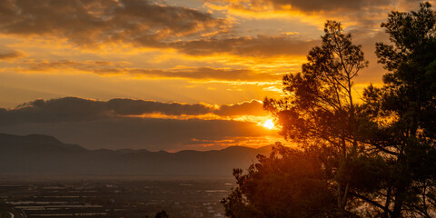 Obraz premium Golden Sunset Over Mountains and Trees with Dramatic Clouds and Fiery Sky
