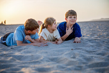 Three children playing with sand on sunset ocean beach. happy family, two school boys and one...