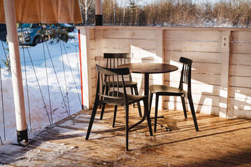 A beautifully crafted wooden table, accompanied by its matching chairs, is elegantly arranged on a serene patio blanketed in fresh, white snow, forming a peaceful and inviting winter scene