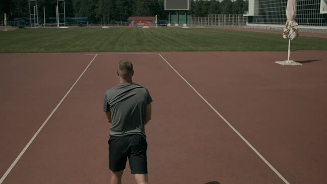 High-angle rear shot of male track and field athlete with acheiria disability, without one hand, aiming, angling then throwing javelin into green grass while improving technique at stadium