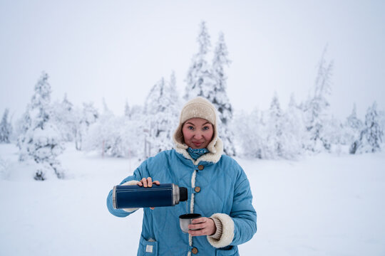 Woman pouring a hot drink from a thermos into a cup in winter forest