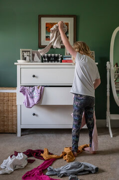 Child sorting clothes in a messy bedroom near a white dresser.