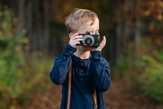 Young boy holding a vintage camera in a forest during autumn. - Powered by Adobe