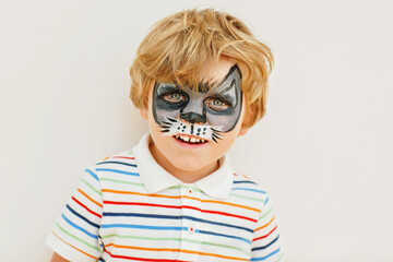 Beautiful little kid boy with face painted with animal or cat, on a birthday party. happy child having fun. Activity for kids on birthday celebration part, face painting, fun and happiness