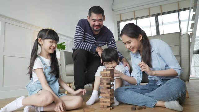 Family relaxing on sofa while kid drawing on floor. Happy Asian little girl enjoy playing a stacking blocks with her parent in living room in free time.